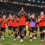 Belgische spelers applaudisseren na afloop op het veld van een verlicht stadion.
