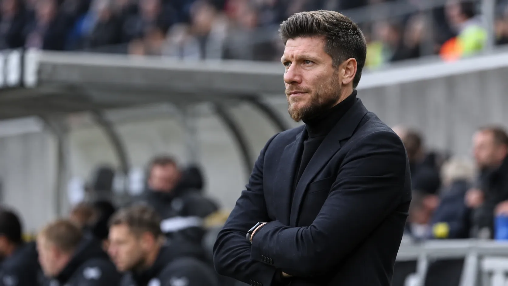 Sébastien Pocognoli staat met gekruiste armen langs de zijlijn van een stadion.