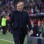 Zinedine Zidane in donker pak langs de zijlijn van een voetbalstadion.