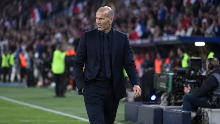 Zinedine Zidane in donker pak langs de zijlijn van een voetbalstadion.