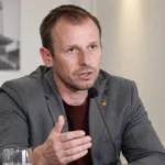 Tom Caluwé spreekt binnenshuis in een microfoon tijdens een clubinterview.