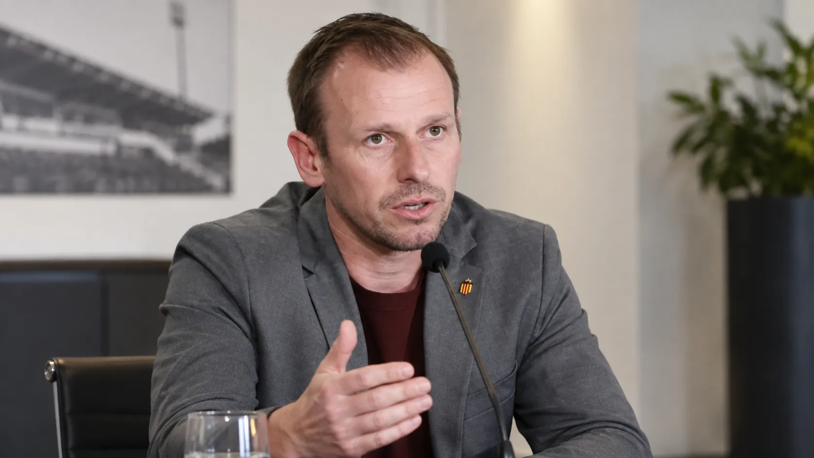 Tom Caluwé spreekt binnenshuis in een microfoon tijdens een clubinterview.