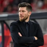 Sébastien Pocognoli in donkere formele kleding in de technische zone van een stadion.