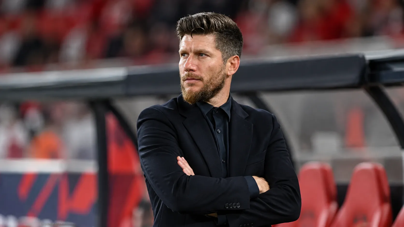 Sébastien Pocognoli in donkere formele kleding in de technische zone van een stadion.