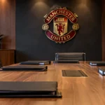 Lege vergaderzaal van Manchester United met een clubembleem aan de wand.