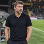 Mark van Bommel staat rustig op de zijlijn van een stadion naast een Belgisch bondslogo.