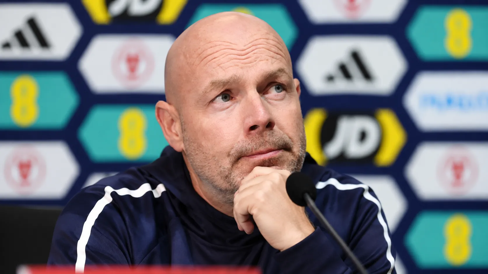 Brian Riemer spreekt op een persconferentie van Denemarken in een trainingsjas.