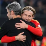 Een speler in een rood voetbalshirt omhelst een staflid na de wedstrijd.