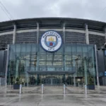 Lege ingang van het Etihad Stadium met een Manchester City-embleem op de gevel.