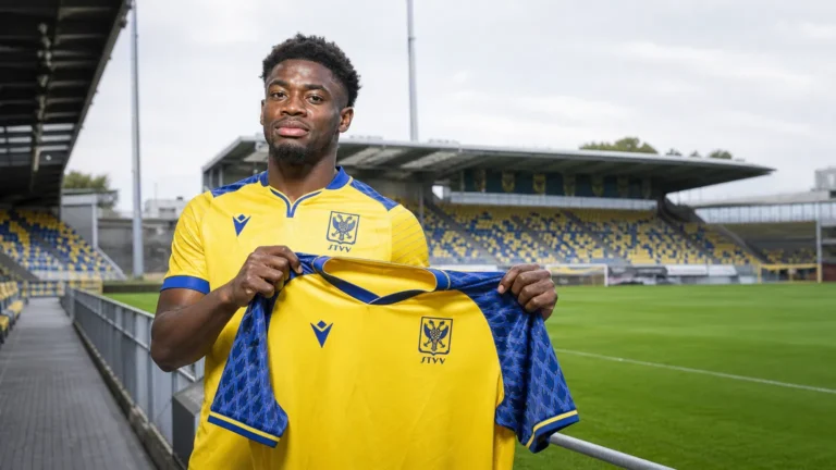 Nathanaël Mbuku poseert met een STVV-shirt tijdens een clubmediapresentatie aan het veld.