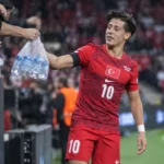 Arda Güler in het Turkse nationale tenue terwijl hij bij een hoekschop een zak water aanneemt.