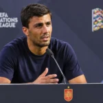 Rodri spreekt op een persconferentie achter een spreekgestoelte met een klein embleem van Spanje.