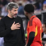 Mark van Bommel in zwarte kledij bij Belgische spelers langs het veld.