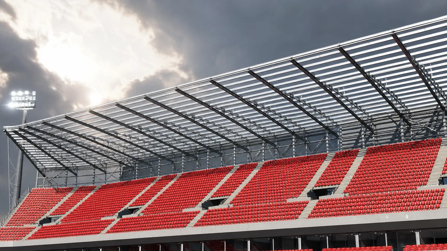Lege tribune met rode zitjes onder de stalen dakconstructie van een stadion.