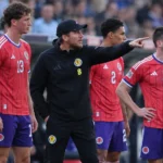 Sébastien Pocognoli staat tussen Schotse spelers langs het veld tijdens een Nations League-wedstrijd.