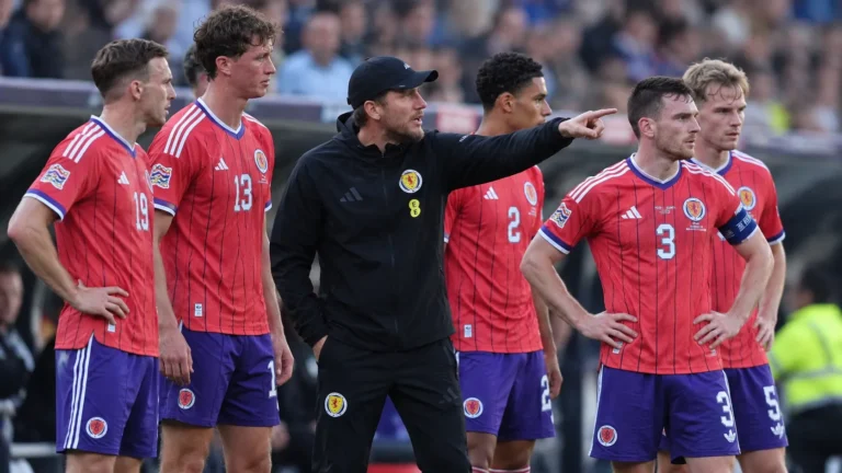 Sébastien Pocognoli staat tussen Schotse spelers langs het veld tijdens een Nations League-wedstrijd.