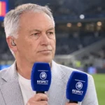 Marc Degryse spreekt als analist met een microfoon in een stadionomgeving.