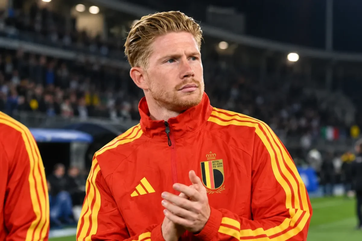 Kevin De Bruyne in een rood trainingsjack van België aan de zijlijn van een stadion.