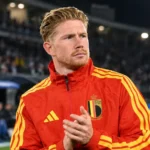 Kevin De Bruyne in een rood trainingsjack van België aan de zijlijn van een stadion.
