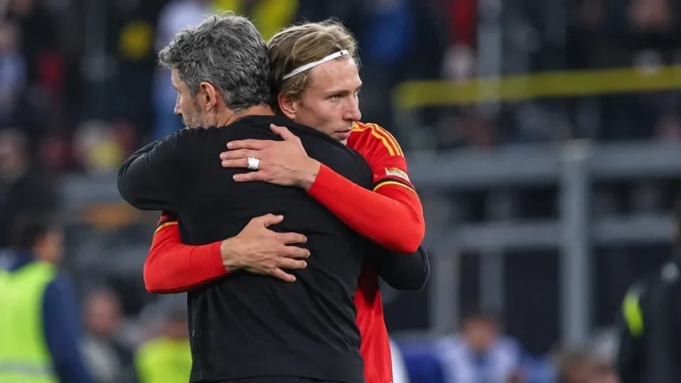 Een Belgische speler in rood omhelst een coach in donkere kleding langs het veld.