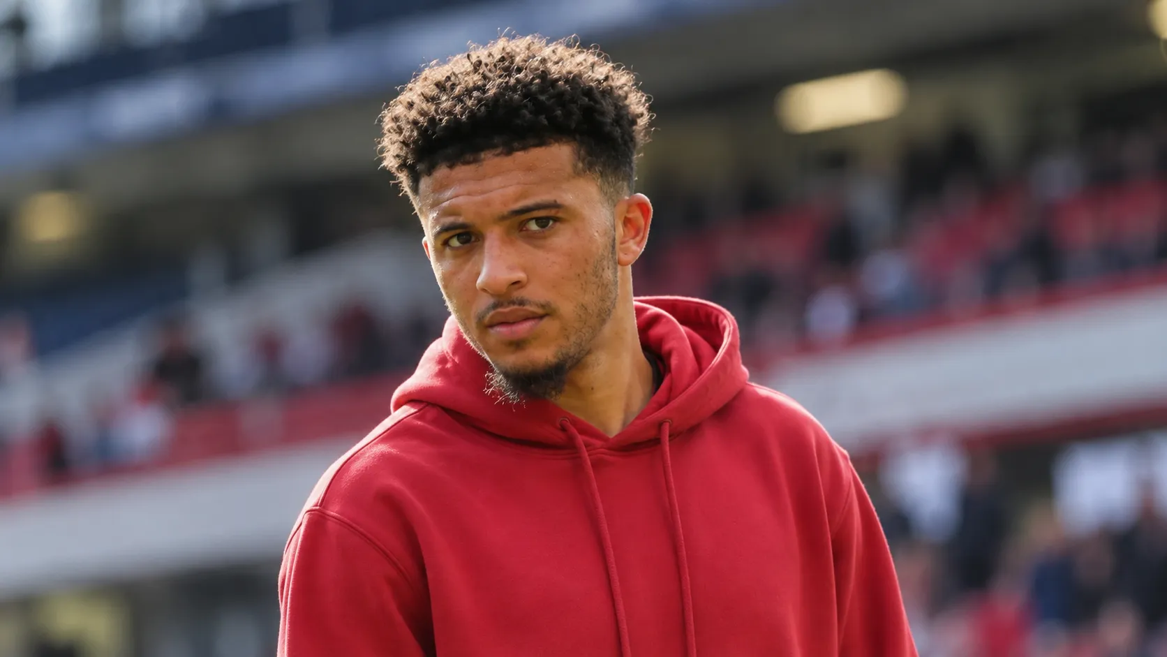 Jadon Sancho in neutrale vrijetijdskleding in een spelerszone van een voetbalstadion.