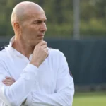 Zinedine Zidane kijkt geconcentreerd toe aan de rand van een trainingsveld.