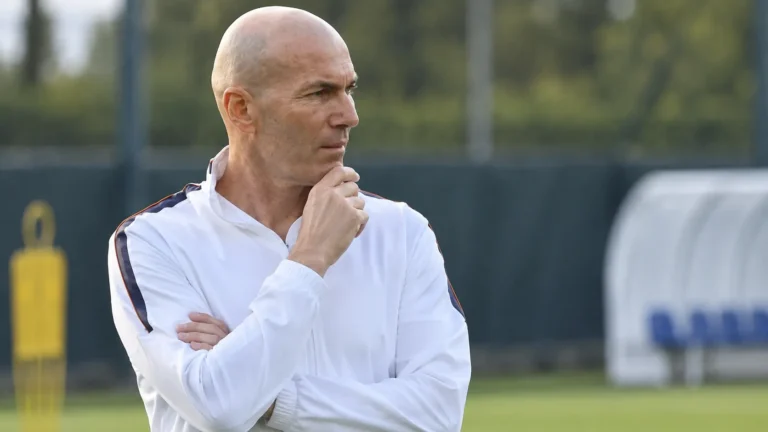 Zinedine Zidane kijkt geconcentreerd toe aan de rand van een trainingsveld.