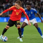 Een Belgische speler in rood dribbelt met de bal terwijl een Italiaanse tegenstander volgt.