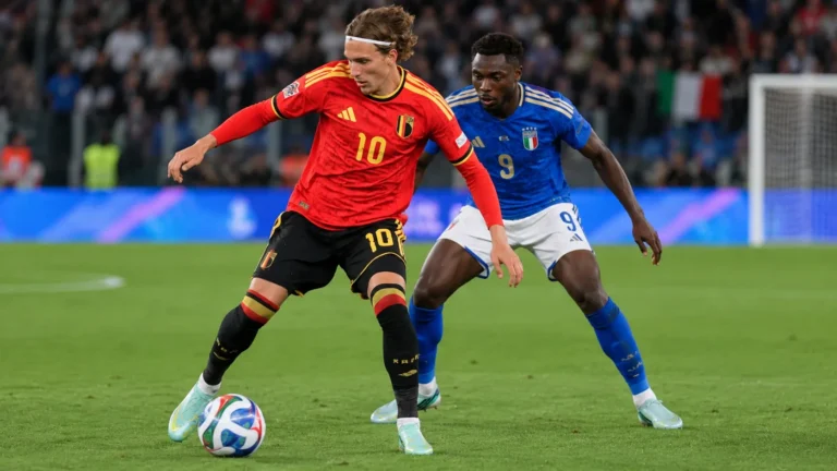 Een Belgische speler in rood dribbelt met de bal terwijl een Italiaanse tegenstander volgt.