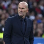 Zinedine Zidane kijkt aandachtig toe aan de zijlijn van een voetbalstadion.