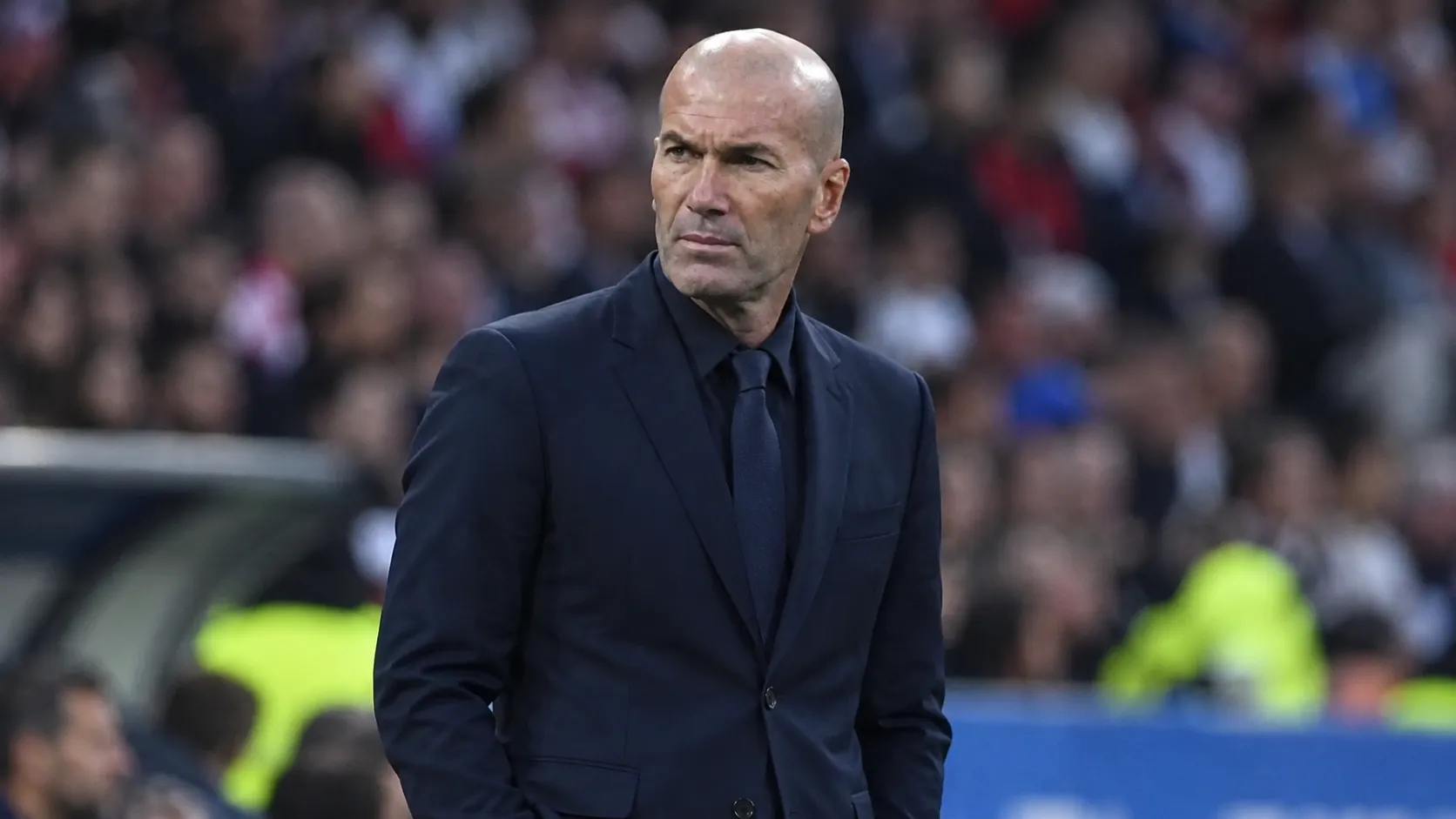 Zinedine Zidane kijkt aandachtig toe aan de zijlijn van een voetbalstadion.