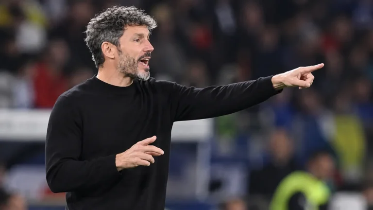 Een coach in zwarte kleding geeft aanwijzingen langs de zijlijn van een interlandstadion.