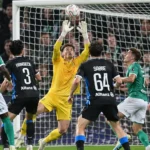 Spelers in groene en donkere tenues verdedigen voor doel in een wedstrijdmoment.