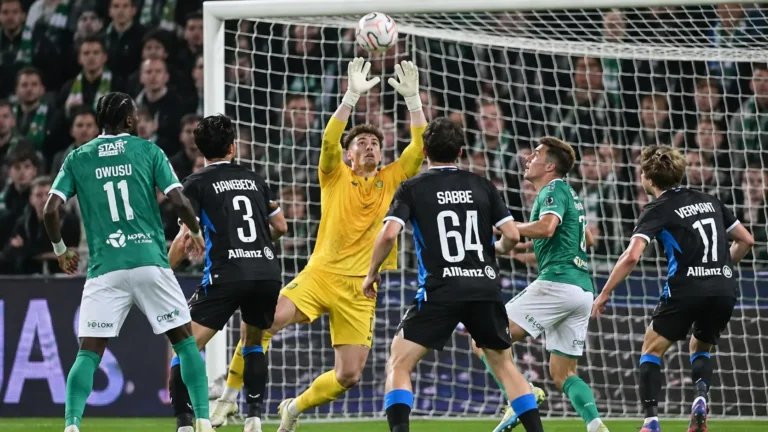 Spelers in groene en donkere tenues verdedigen voor doel in een wedstrijdmoment.
