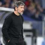 Mark van Bommel in zwarte kleding langs de zijlijn bij een wedstrijd van België.