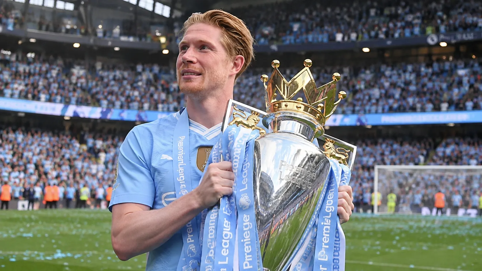 Een speler in lichtblauw tenue houdt een grote trofee vast in een gevuld stadion.