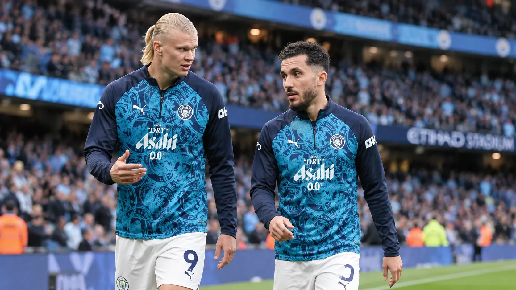 Twee voetballers in blauwe opwarmkleding op het veld van een stadion.