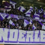 Een volle tribune met Anderlecht-supporters die paars-witte vlaggen tonen.