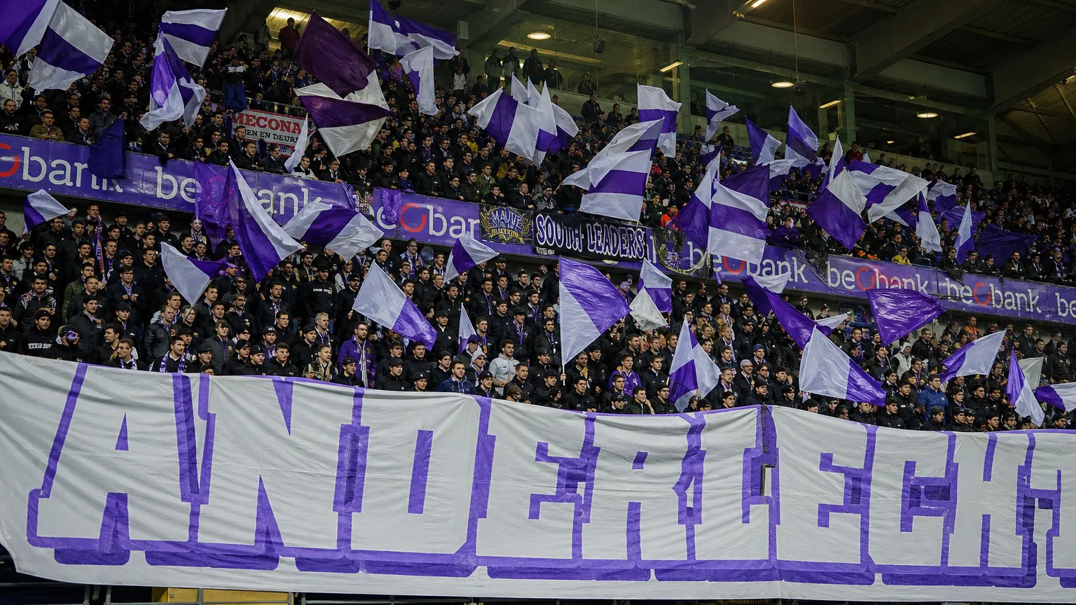 Een volle tribune met Anderlecht-supporters die paars-witte vlaggen tonen.