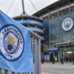Een lichtblauwe vlag van Manchester City aan een stadioningang.