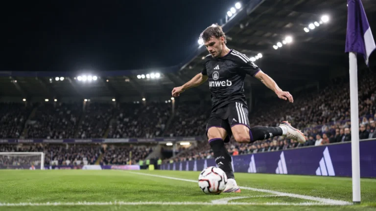 Lukas Ambros trapt een bal tijdens een wedstrijd van RSC Anderlecht onder de stadionlichten.