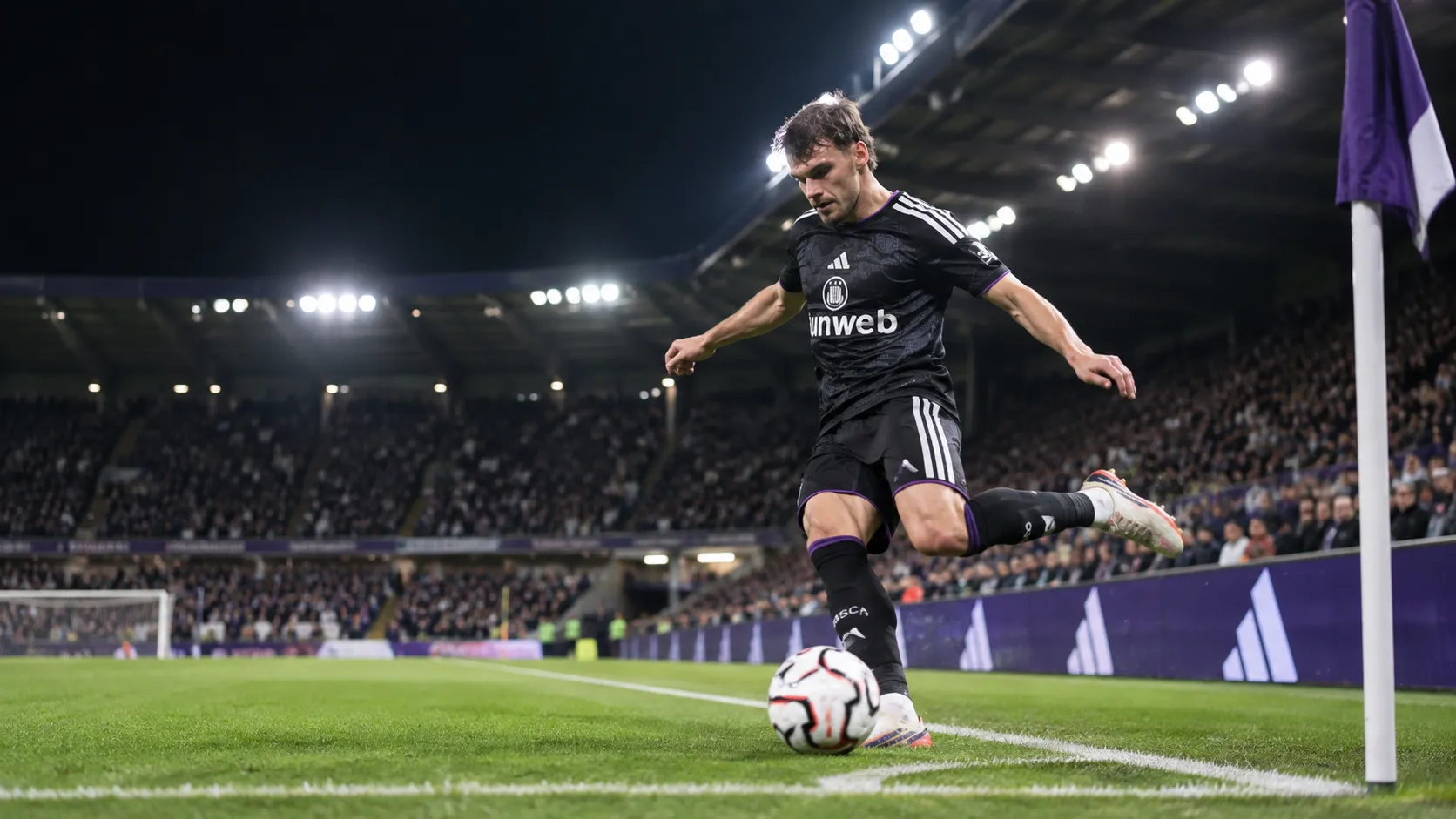Lukas Ambros trapt een bal tijdens een wedstrijd van RSC Anderlecht onder de stadionlichten.