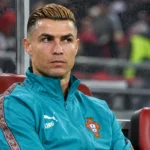 Cristiano Ronaldo in Portugal-trainingsjas op de spelersbank tijdens een interland.