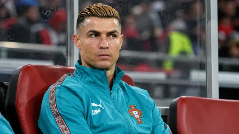 Cristiano Ronaldo in Portugal-trainingsjas op de spelersbank tijdens een interland.