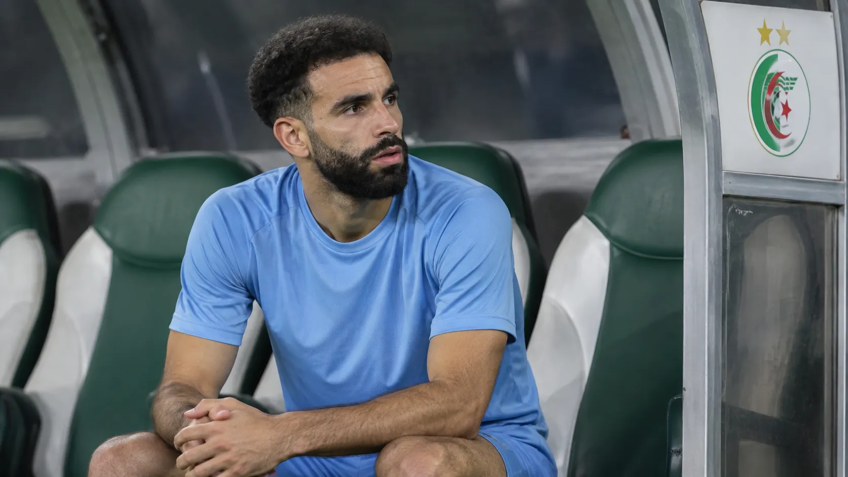 Rayan Aït-Nouri zit alleen op de bank van Algerije in neutrale sportkleding.