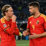 Twee Belgische spelers in rode nationale tenues overleggen op het veld na een wedstrijd.