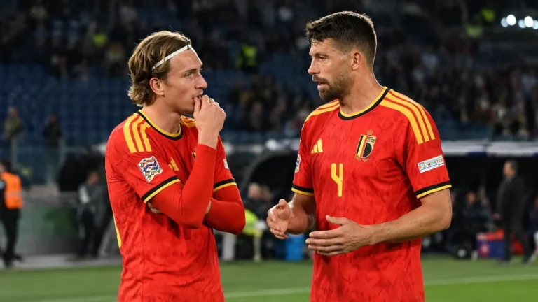 Twee Belgische spelers in rode nationale tenues overleggen op het veld na een wedstrijd.