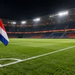 Een leeg verlicht voetbalveld met een Nederlandse vlag aan de hoekvlag na een wedstrijd.