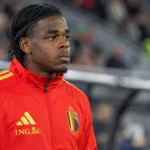 Een Belgische verdediger in een rode trainingsjas van de nationale ploeg langs het veld.