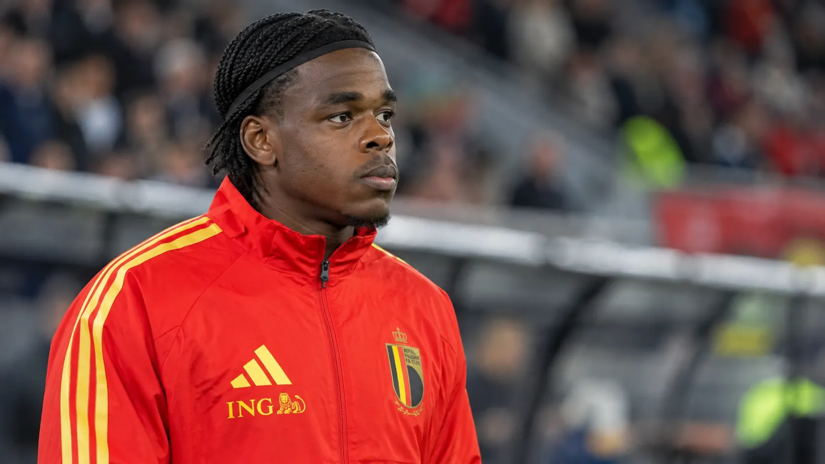 Een Belgische verdediger in een rode trainingsjas van de nationale ploeg langs het veld.